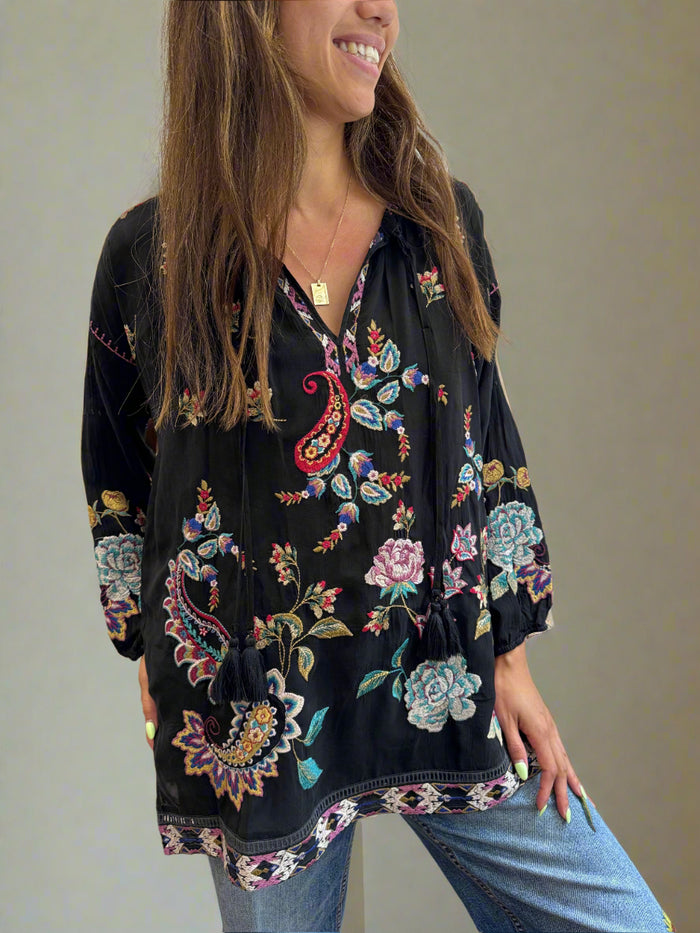 Woman wearing a black embroidered jacket with colorful floral patterns.