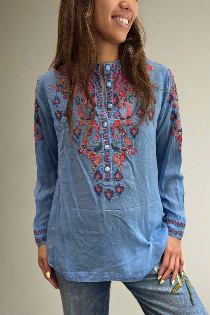 Woman wearing a blue embroidered long-sleeve top against a white background