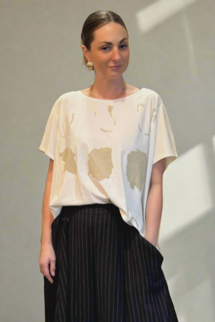 Woman wearing a white patterned top and black pleated skirt in an indoor setting.