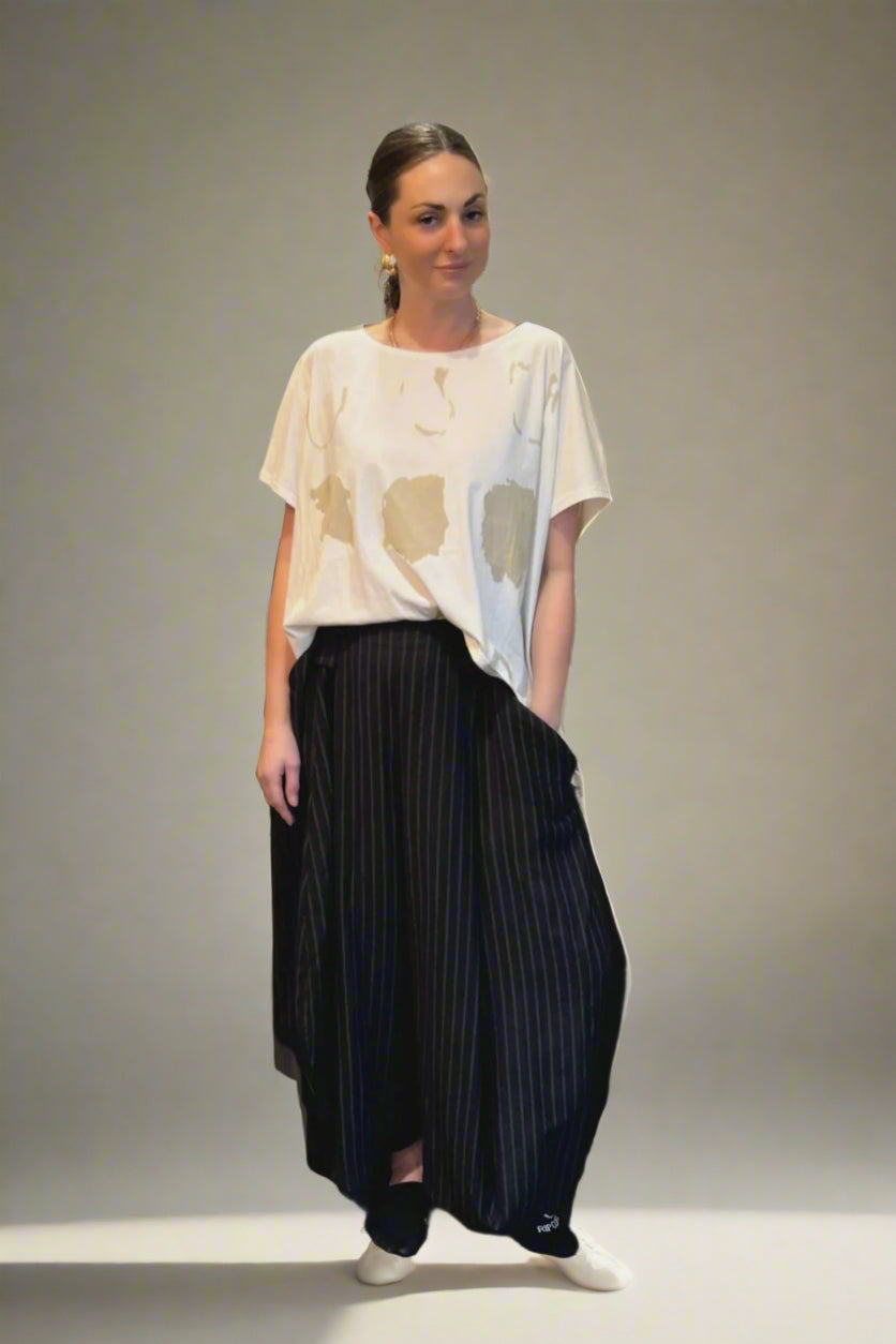 Woman in a white top and black skirt standing in a room with decorative pillows and a water bottle on a table.