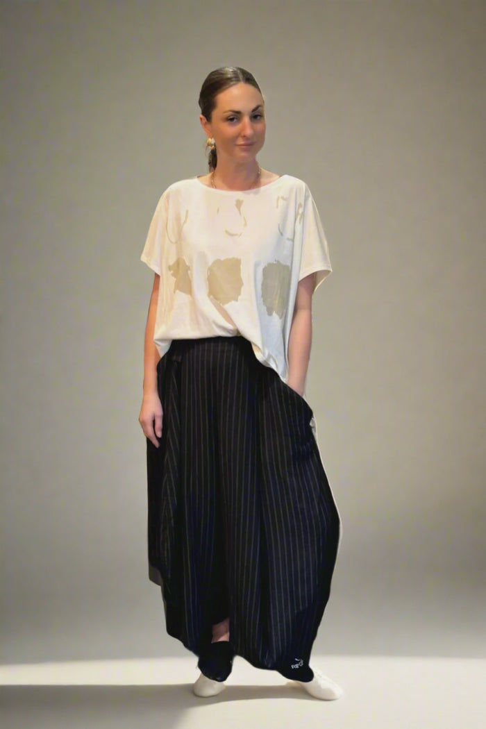 Woman in a white top and black skirt standing in a room with decorative pillows and a water bottle on a table.