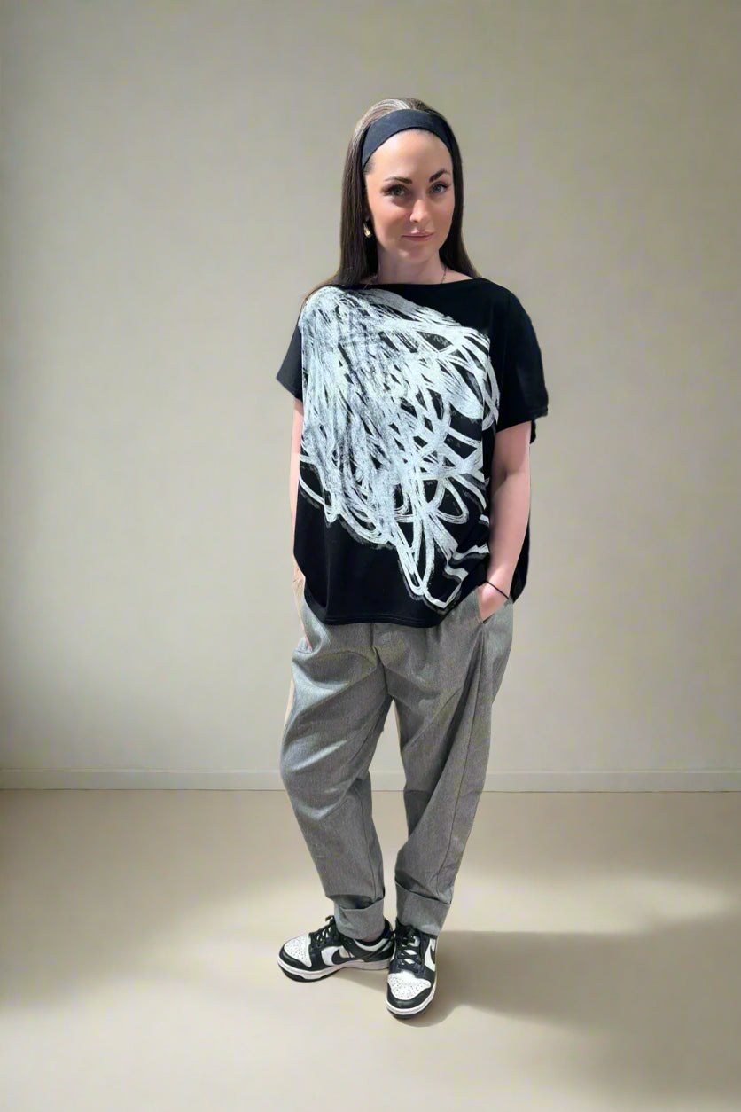 Person wearing a black t-shirt with white design, gray pants, and black and white sneakers in a store setting.