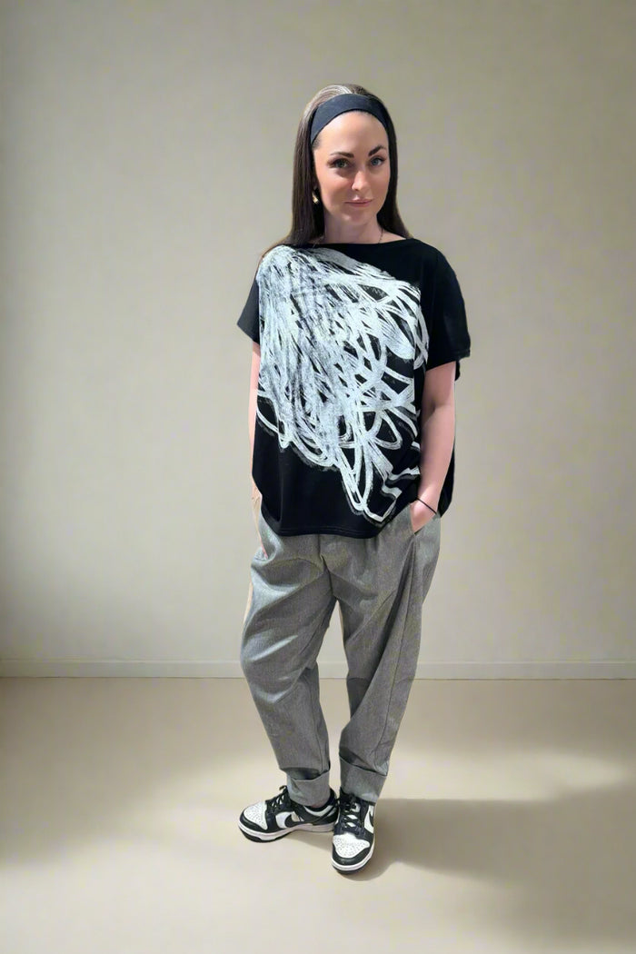 Person wearing a black t-shirt with white design, gray pants, and black and white sneakers in a store setting.
