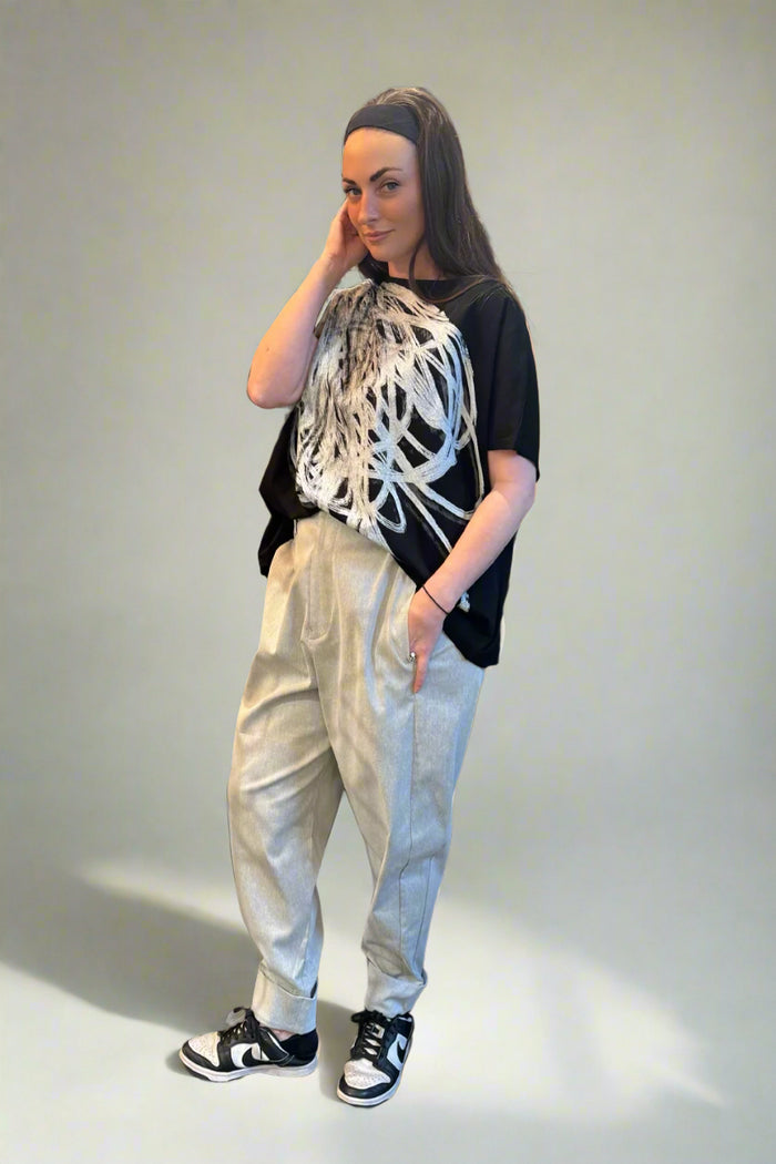 Person wearing a black t-shirt with white abstract design, light-colored pants, and black sneakers in a clothing store.