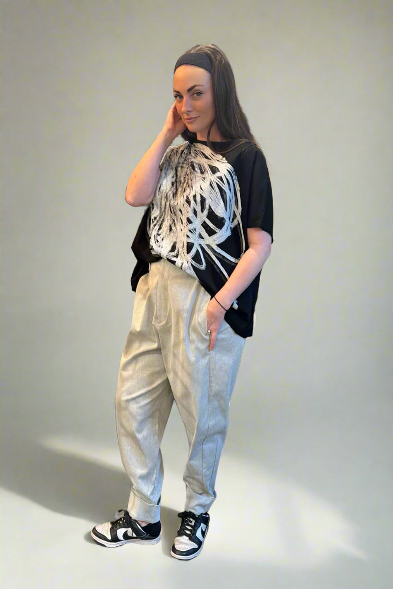 Person wearing a black t-shirt with white abstract design, light-colored pants, and black sneakers in a clothing store.